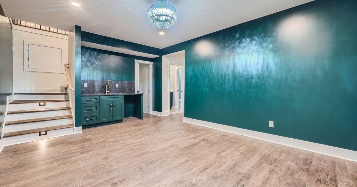 Finished basement with teal walls, wet bar, wood-look flooring, and illuminated staircase in Atlanta, GA.