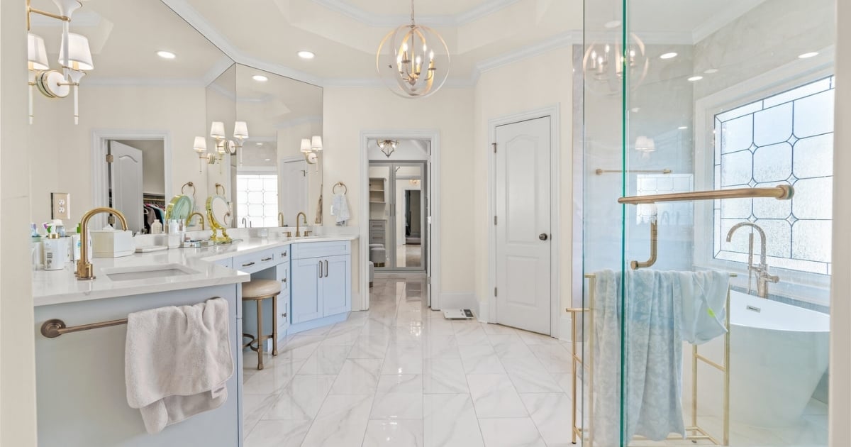 Primary bathroom with light blue vanities, marble tile, glass shower, freestanding tub, and brass fixtures in Atlanta, GA.