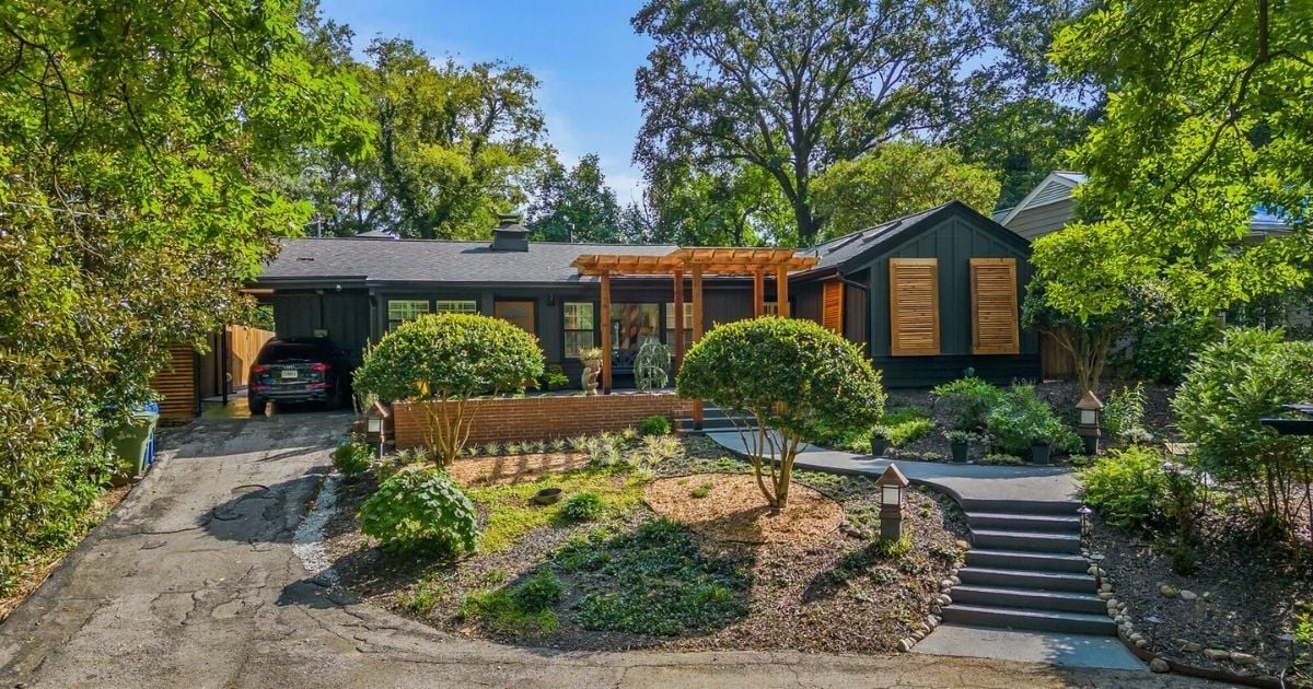 Dark home exterior with wood shutters, pergola, landscaped front yard, and garden walkway in Atlanta, GA.