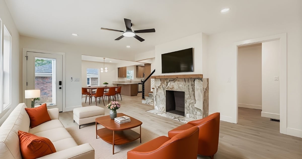 Open-concept living room with stone fireplace, orange seating, and adjoining dining area and kitchen in Atlanta, GA.