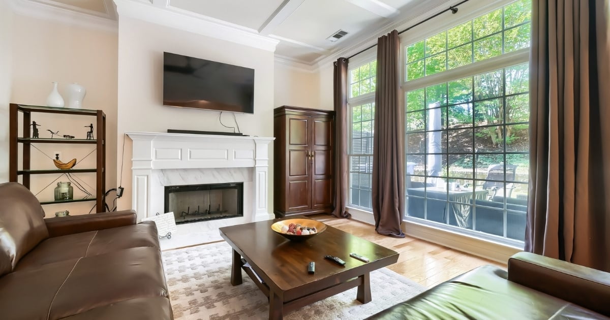 Living room with white fireplace, leather seating, wood coffee table, and large windows overlooking the backyard in Atlanta, GA.