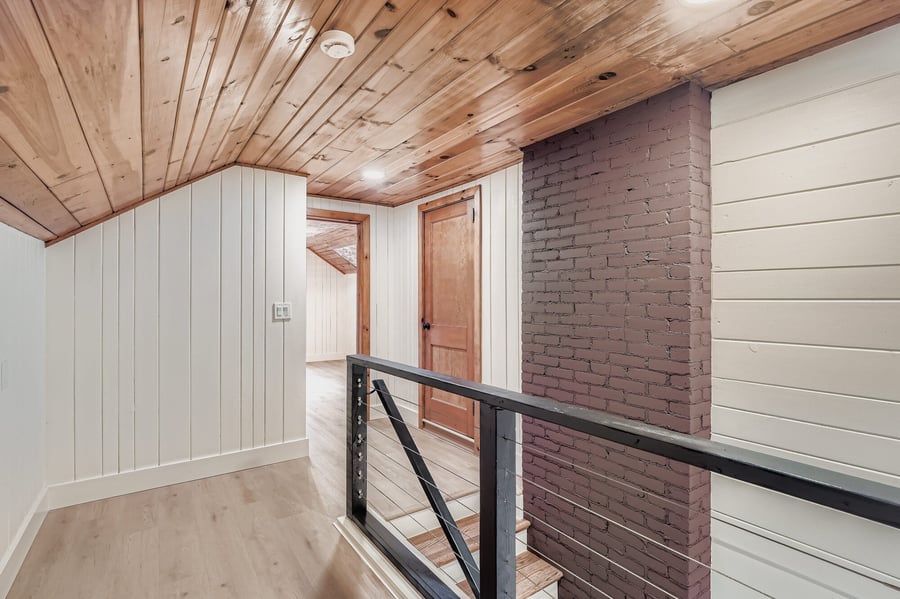 Upstairs hall with a wood ceiling, black railing and brick wall